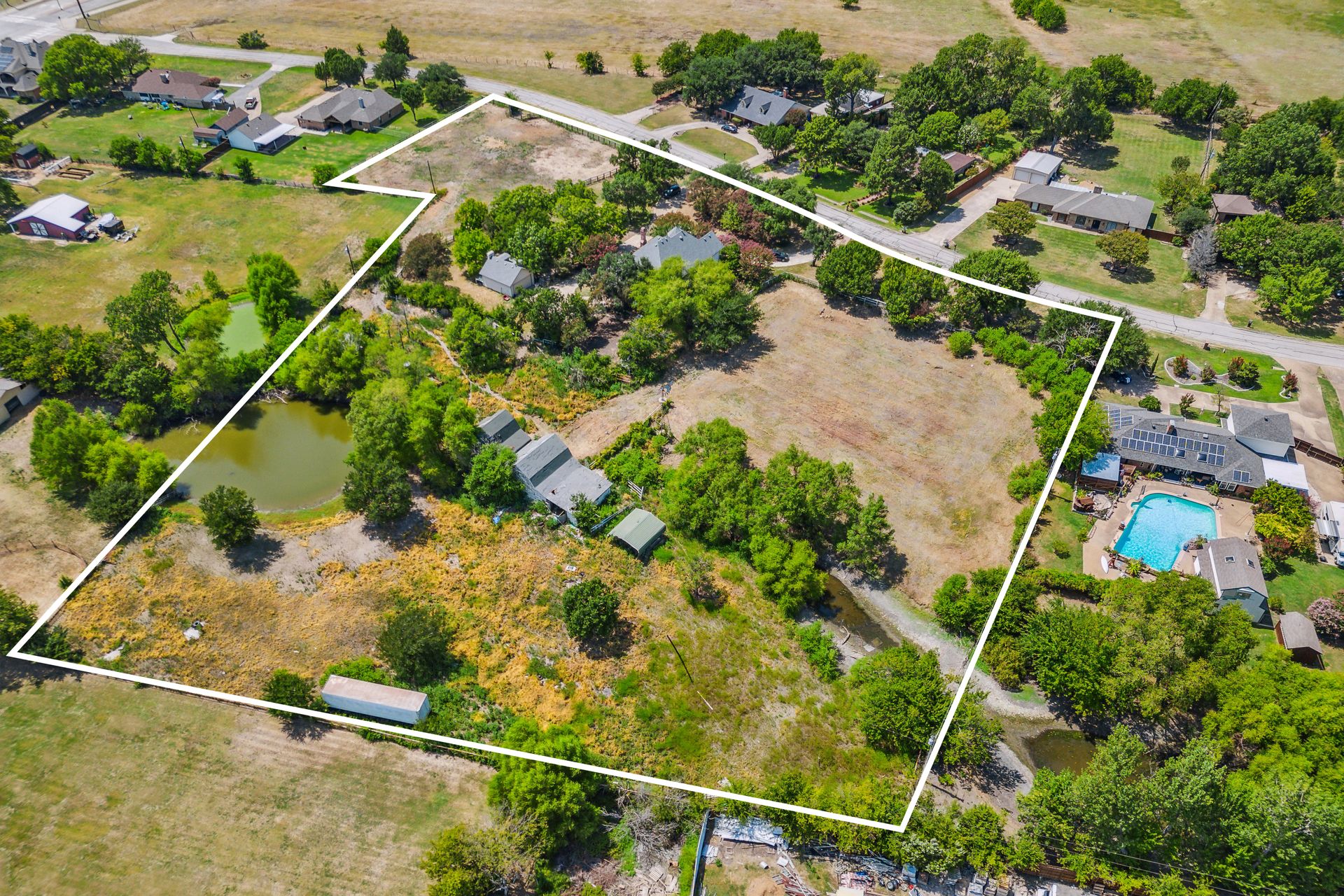 Aerial view of the 2.48-acre 3706 Castle Drive estate compound in Rowlett, Texas, showing the main residence, cabin, workshop, two barns, pond, and circular drive within a fenced boundary.